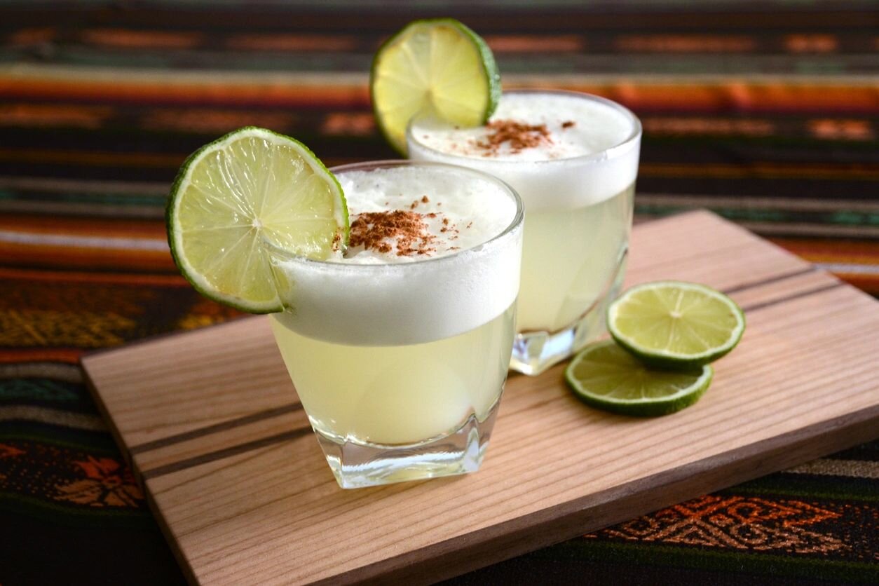 Two glasses of drink with lime and cinnamon on a wooden board.