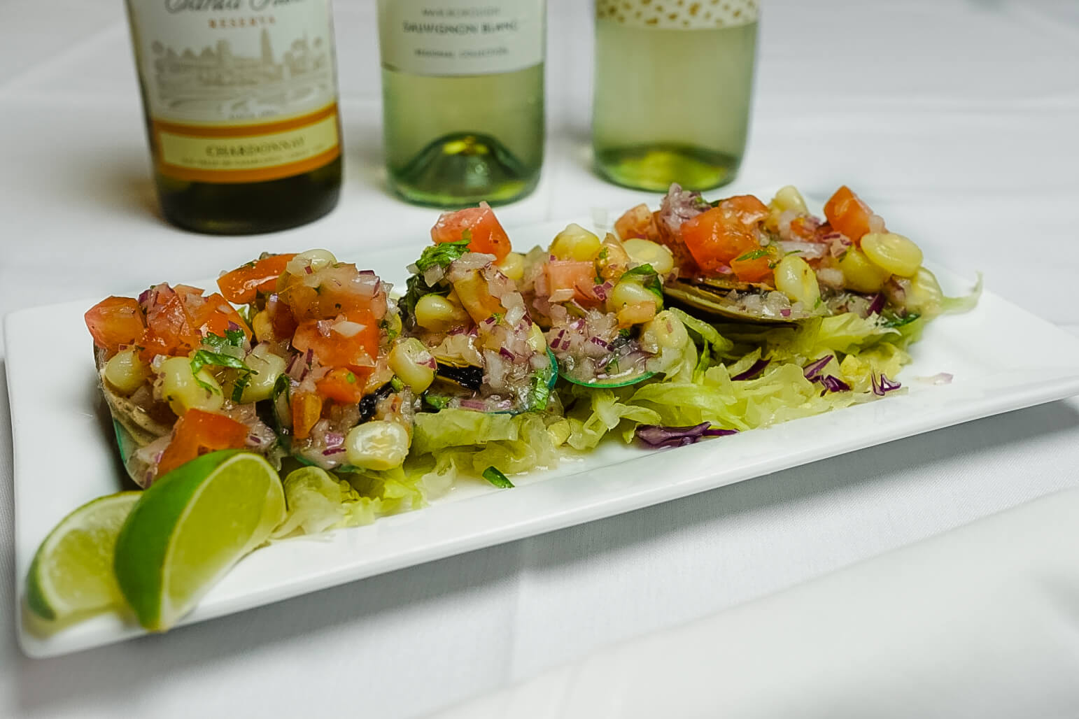 A white plate topped with salad next to two bottles of wine.