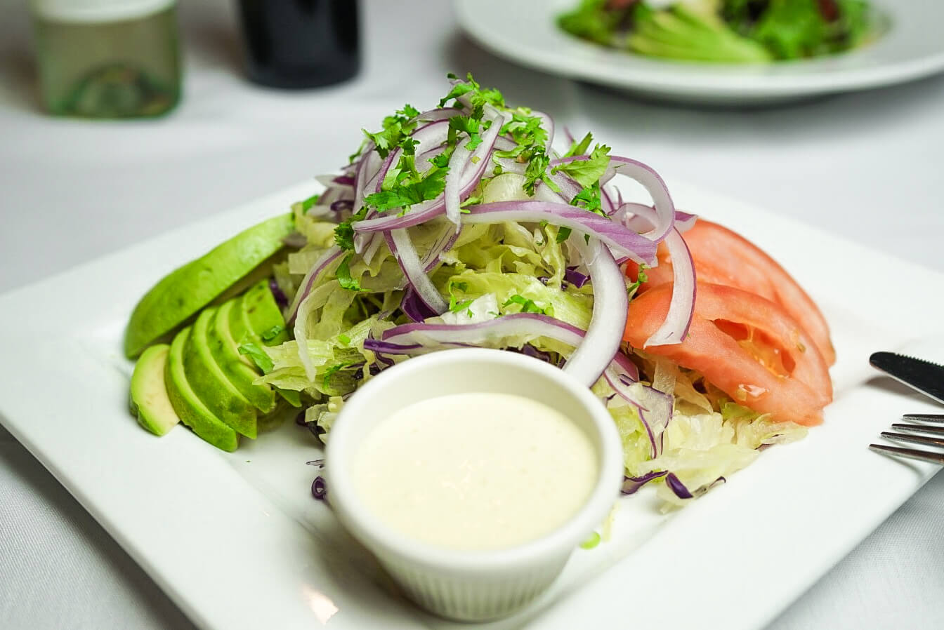 A plate of salad with dressing on the side.